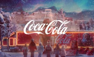 A magical winter scene featuring children watching a glowing Coca-Cola Christmas truck pass through a snowy village with a giant glass bottle silhouette in the center.